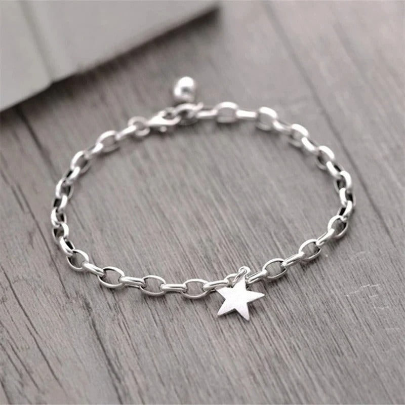Silver chain bracelet with a star charm on a wooden surface