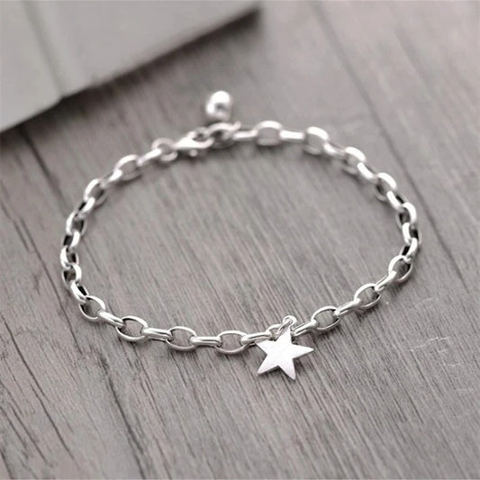 Silver chain bracelet with a star charm on a wooden surface