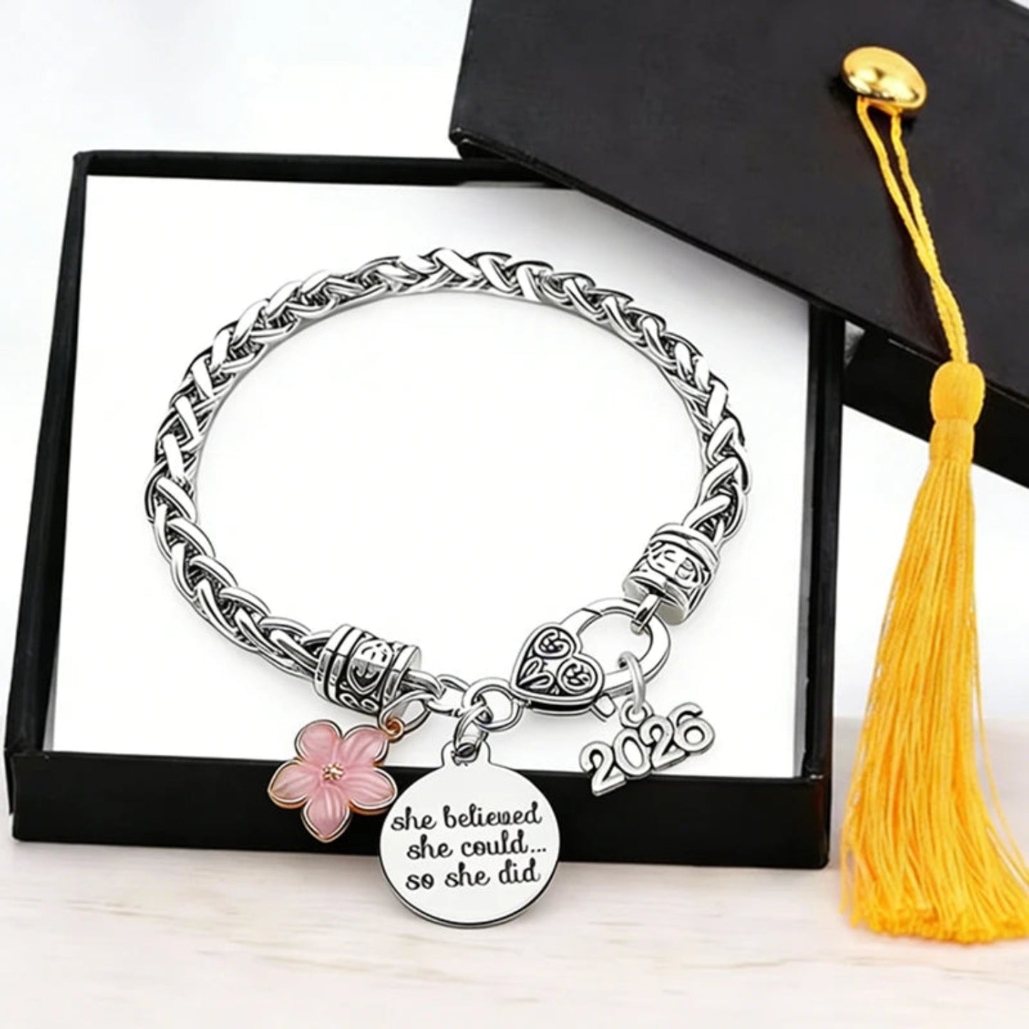 Silver bracelet with charms and '2026' on a white background with a yellow tassel.