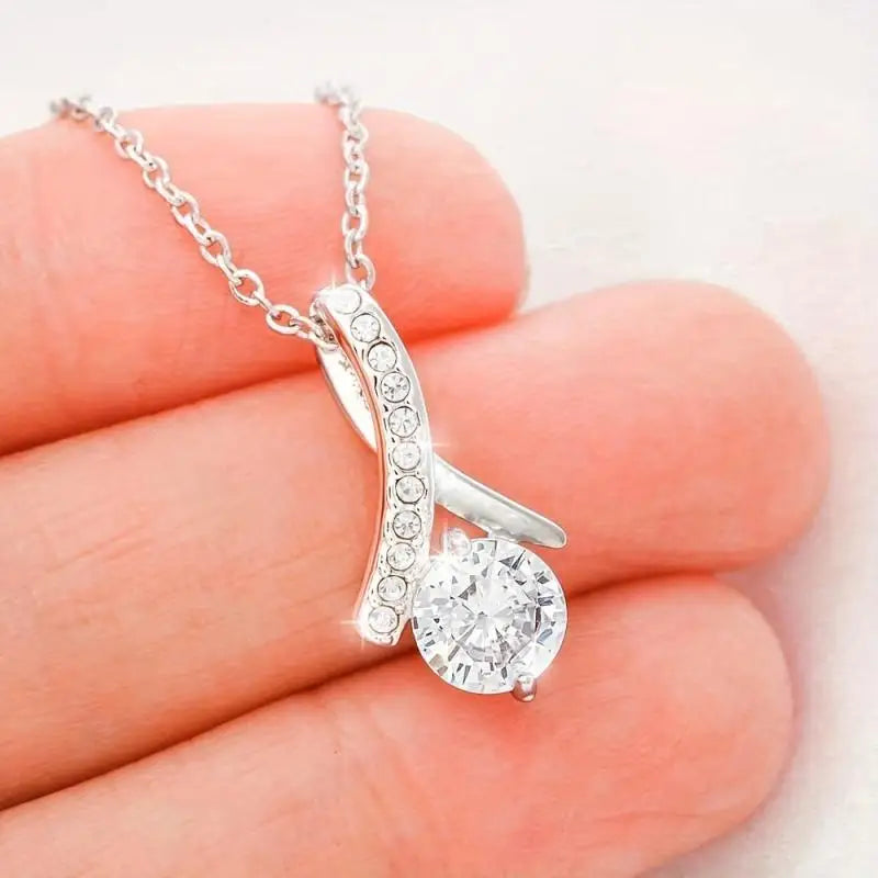 Silver necklace with a pendant held between fingers on a light background
