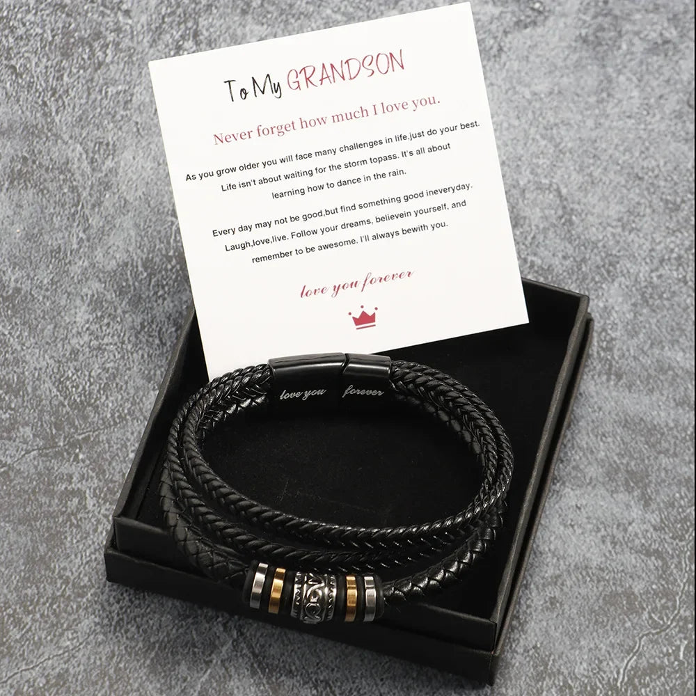 Black braided leather bracelet with gold accents in a box with a card on a gray textured background