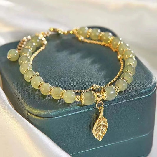 Beaded bracelet with a gold leaf charm on a teal jewelry box