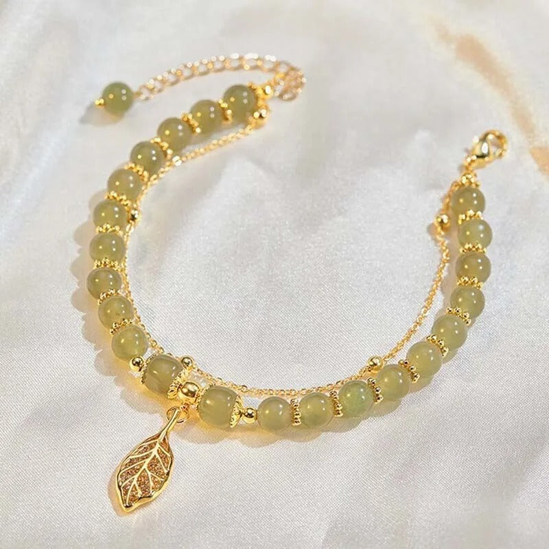 Bracelet with green beads and a gold leaf charm on a white background