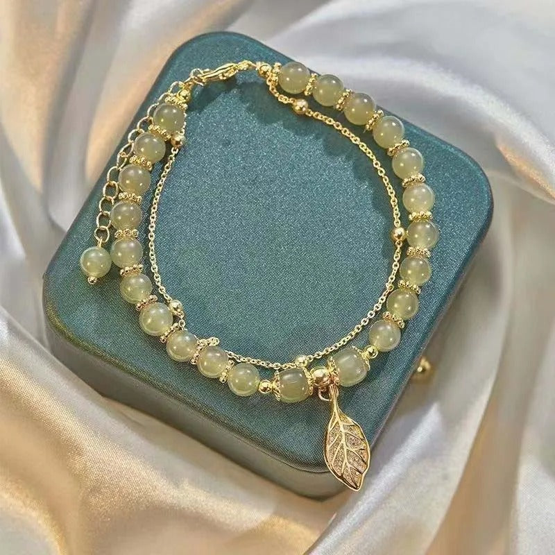 Beaded bracelet with a leaf charm on a teal box against a satin background