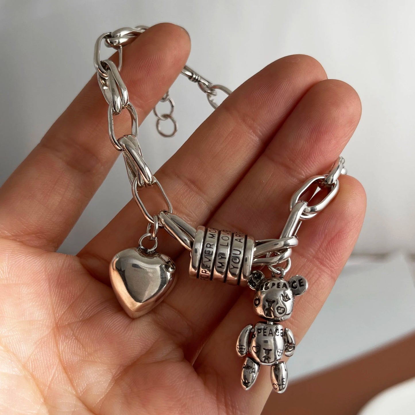 Silver bracelet with charms held in a hand against a neutral background
