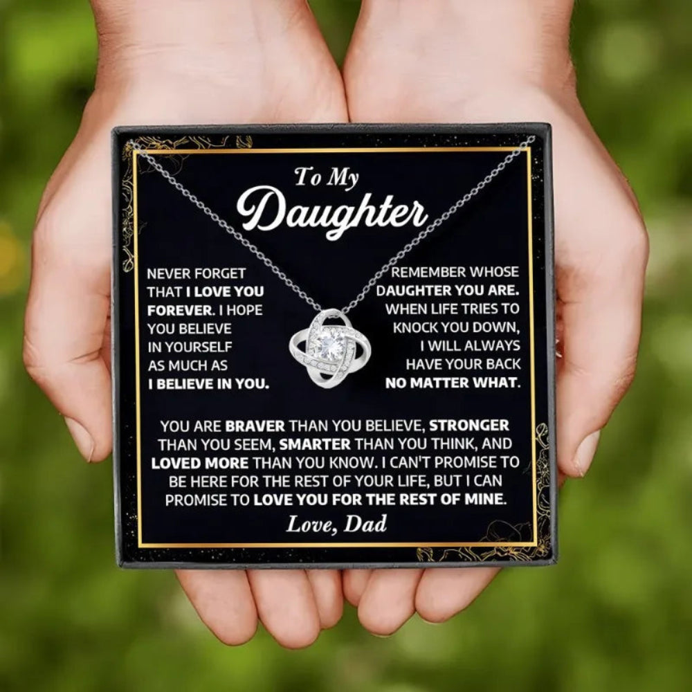 Plaque with a message to a daughter and a necklace, held by hands against a blurred green background.