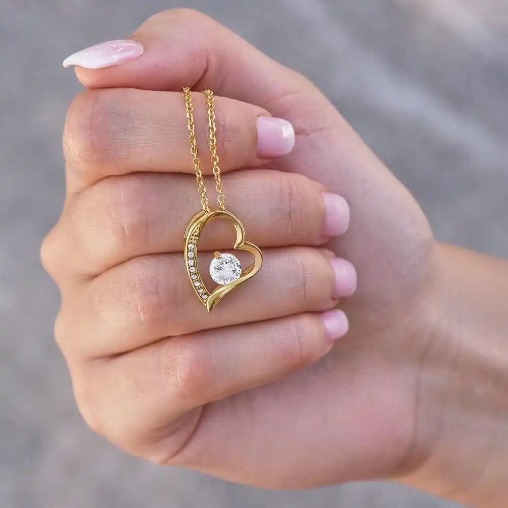 Gold heart-shaped necklace with a diamond held in a hand against a neutral background