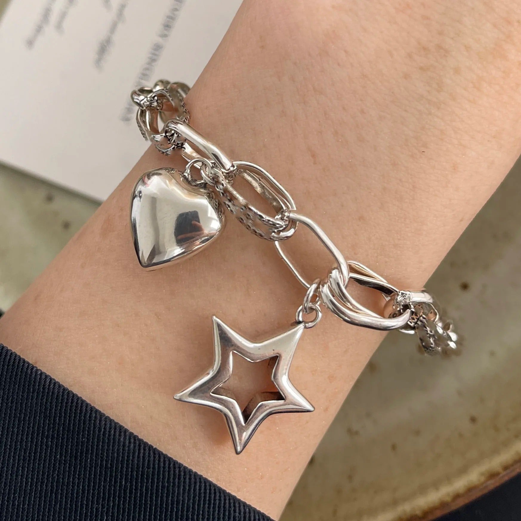 Silver bracelet with heart and star charms on a wrist.