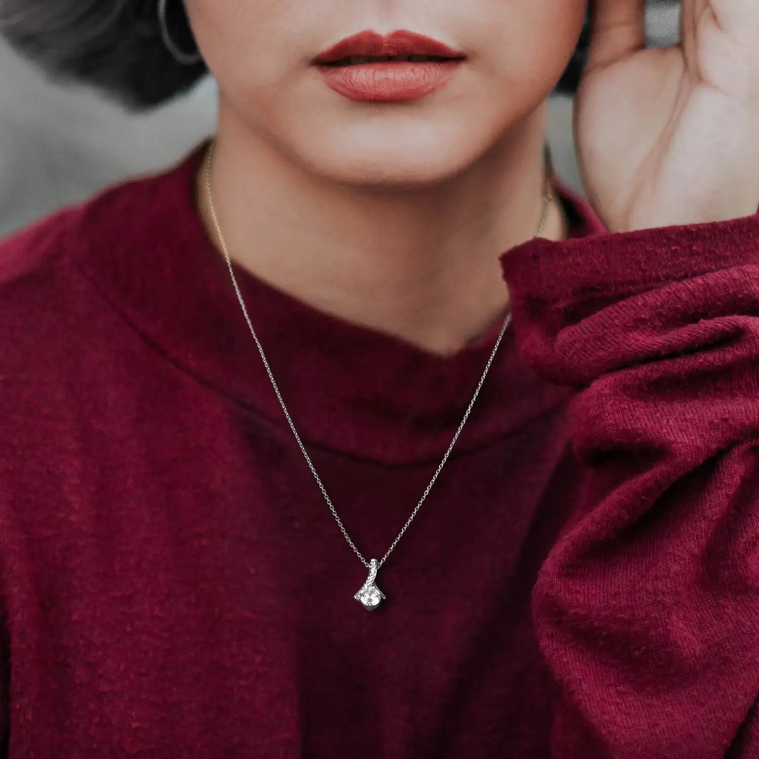 Person wearing a maroon sweater with a silver necklace featuring a pendant.