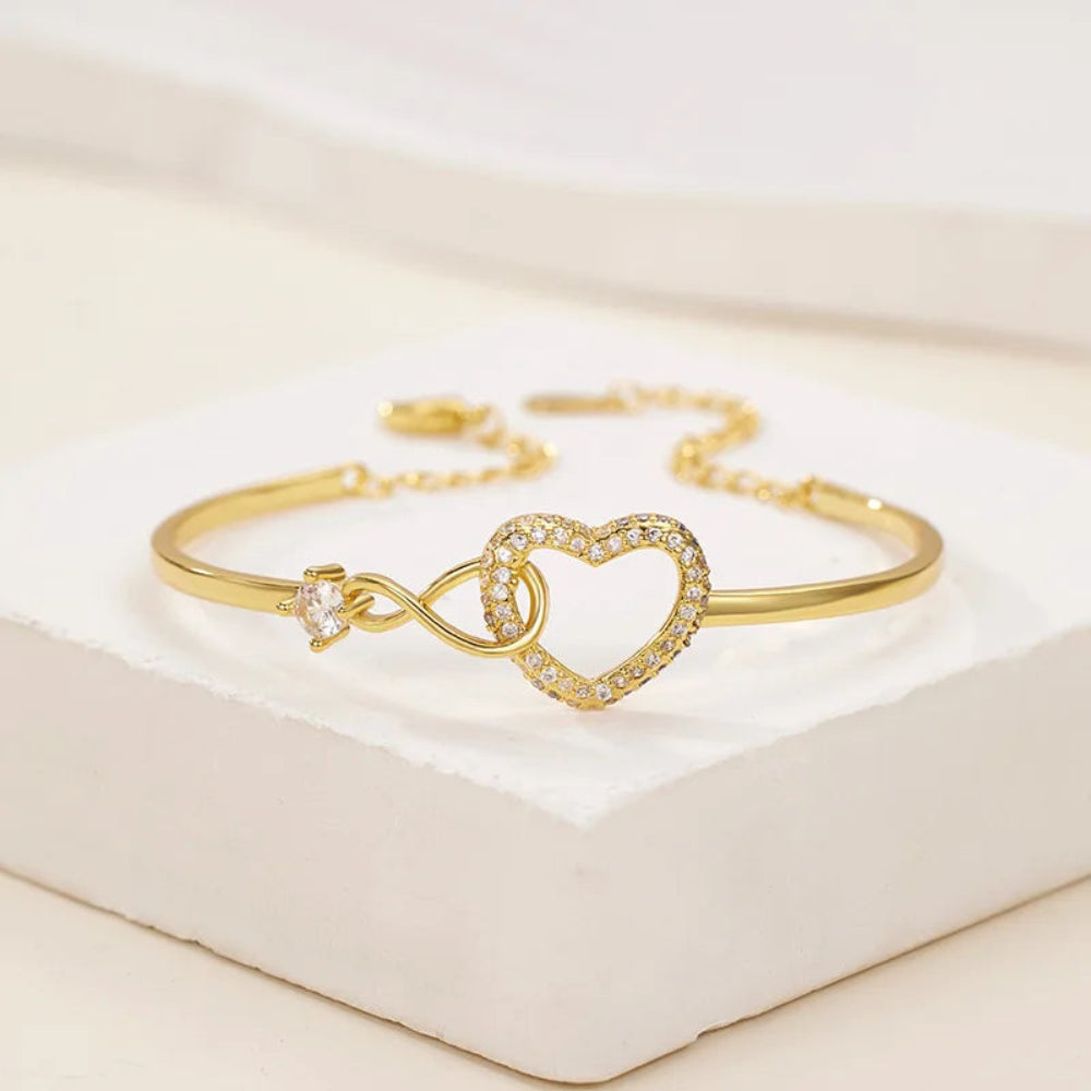Gold bracelet with heart and infinity symbol on a light background