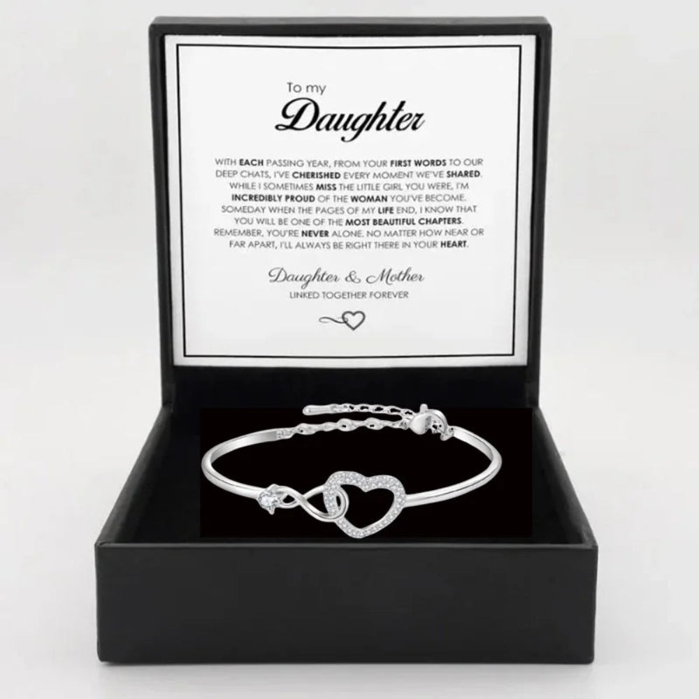 Silver bracelet with heart design in a black box with a message card, on a light gray background