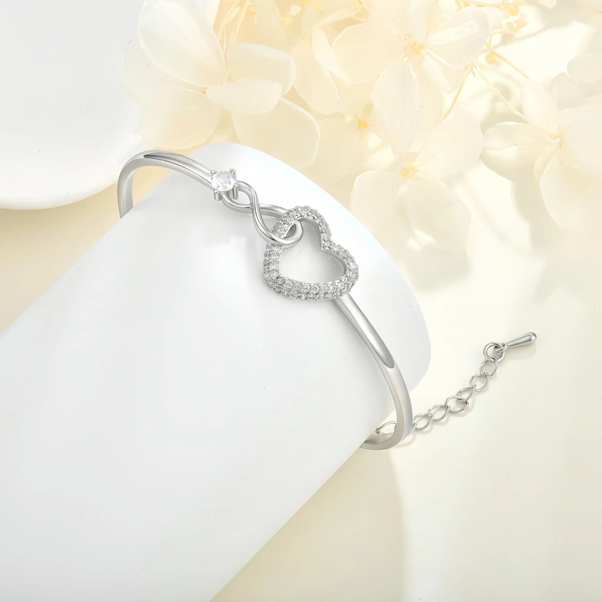 Silver bracelet with a heart-shaped clasp on a white surface with light flowers in the background