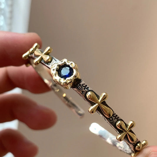 Gold and silver bracelet with a blue gemstone held by a hand against a neutral background