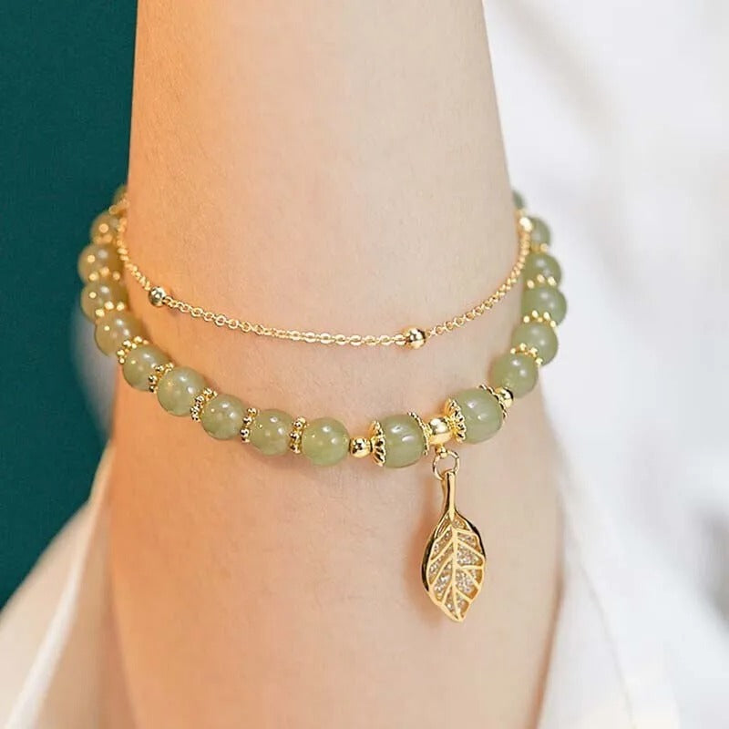 Green beaded bracelet with a leaf charm on a wrist against a white background