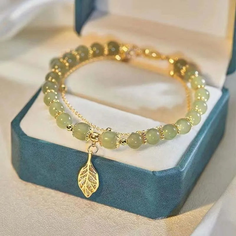Green beaded bracelet with a gold leaf charm on a blue jewelry box