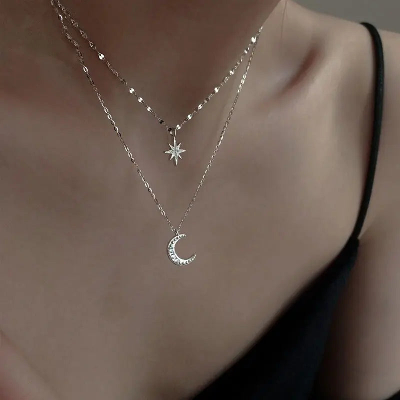 Silver necklace with star and moon pendants on a person wearing a black top.