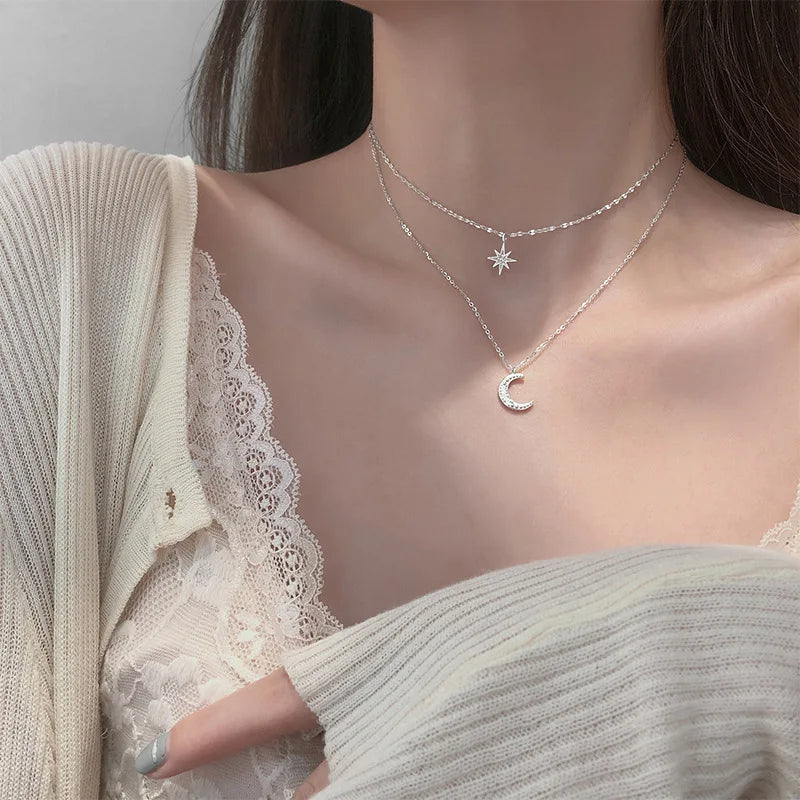 Woman wearing a delicate silver necklace with a moon pendant against a neutral background