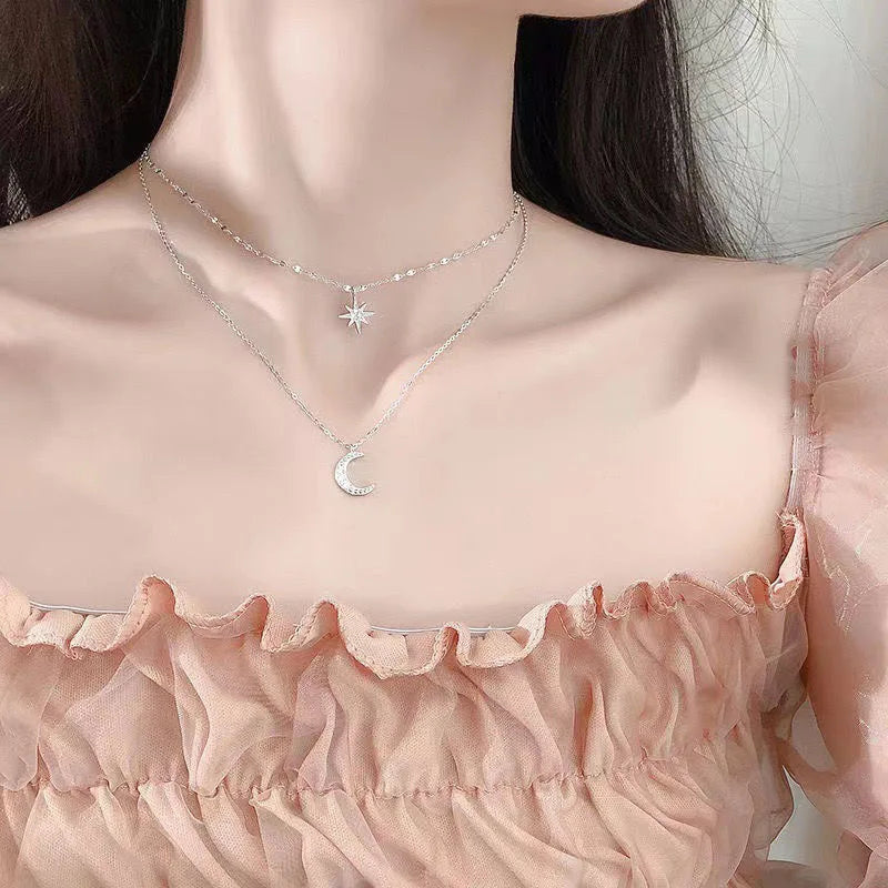 Person wearing a delicate silver necklace with star and moon pendants on a light background
