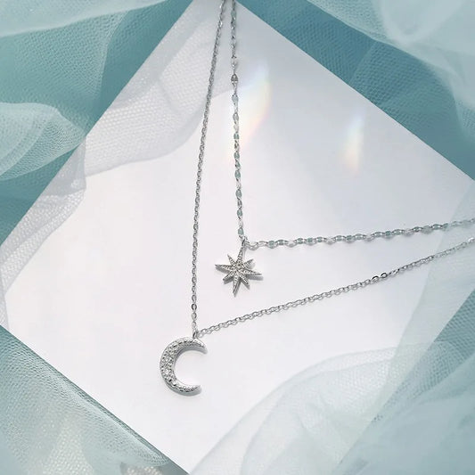 Silver necklace with star and moon pendants on a light fabric background