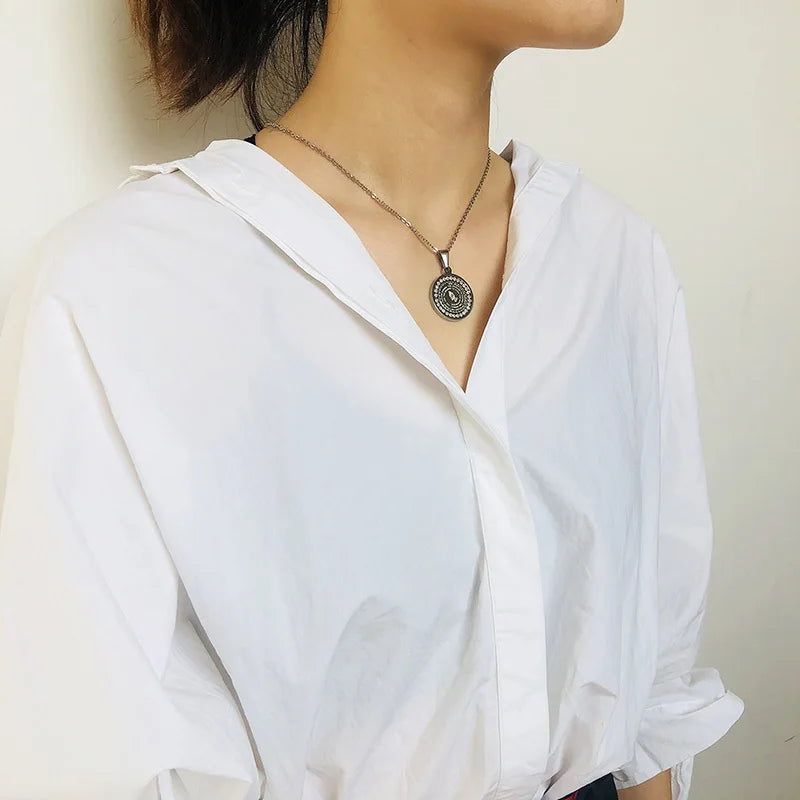 Person wearing a white shirt with a necklace featuring a circular pendant.