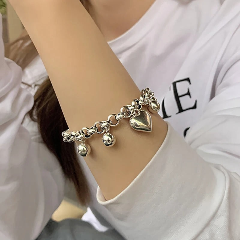 Silver bracelet with heart and ball charms on a person's arm.