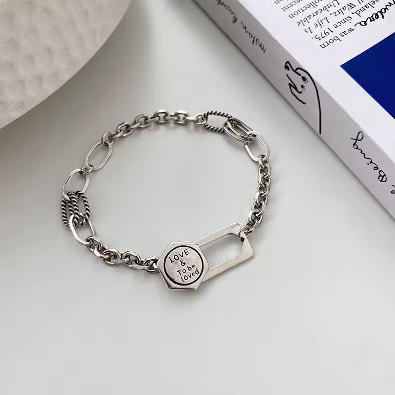Silver chain bracelet with a heart-shaped tag on a light gray surface.
