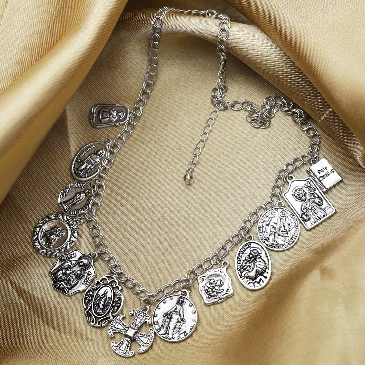 Silver necklace with various religious charms on a beige fabric background