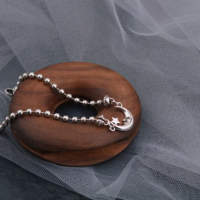 Silver bracelet with moon and star charm on a wooden block against a gray fabric background