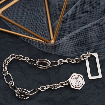 Silver chain bracelet with a hexagonal tag on a dark fabric background