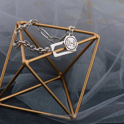 Silver bracelet with a heart-shaped charm on a geometric bronze stand against a gray background