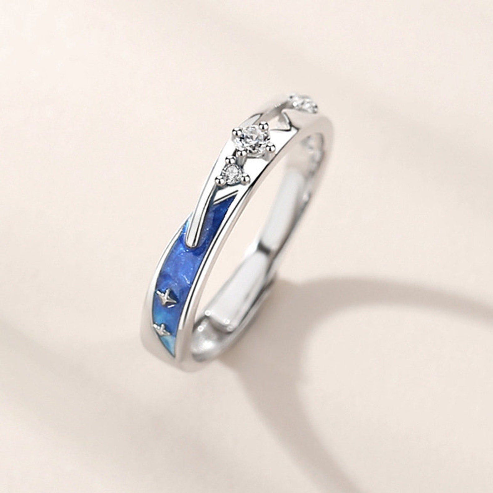 Silver ring with blue inlay and diamond accents on a beige background