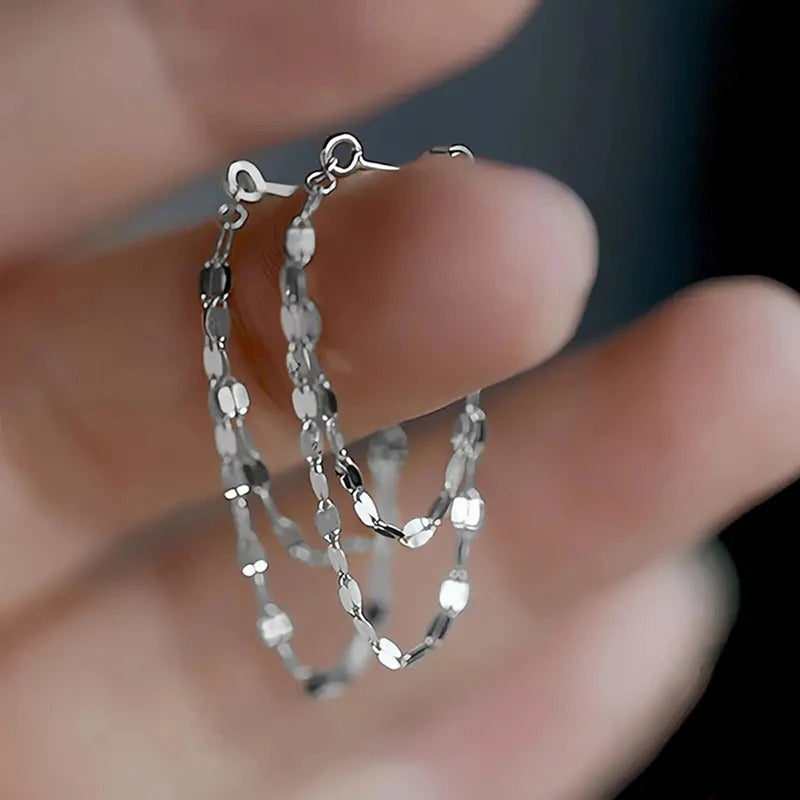 Silver chain necklace held between fingers against a blurred background