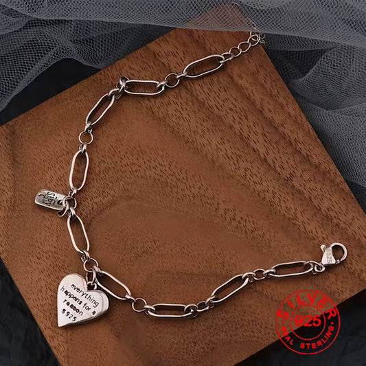 Silver bracelet with heart-shaped charm and tag on a wooden platform