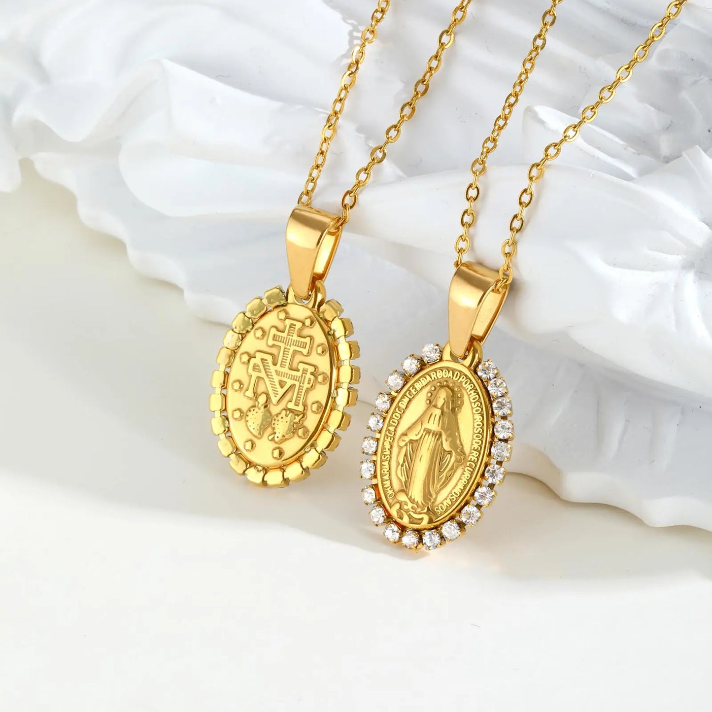 Two gold necklaces with religious pendants on a white shell background