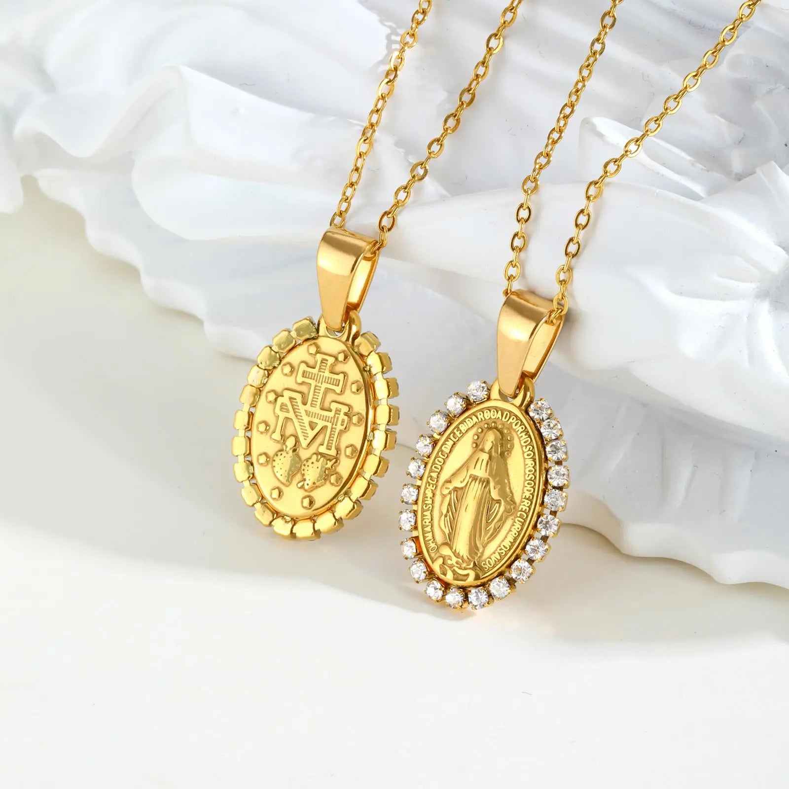 Two gold necklaces with religious pendants on a white shell background