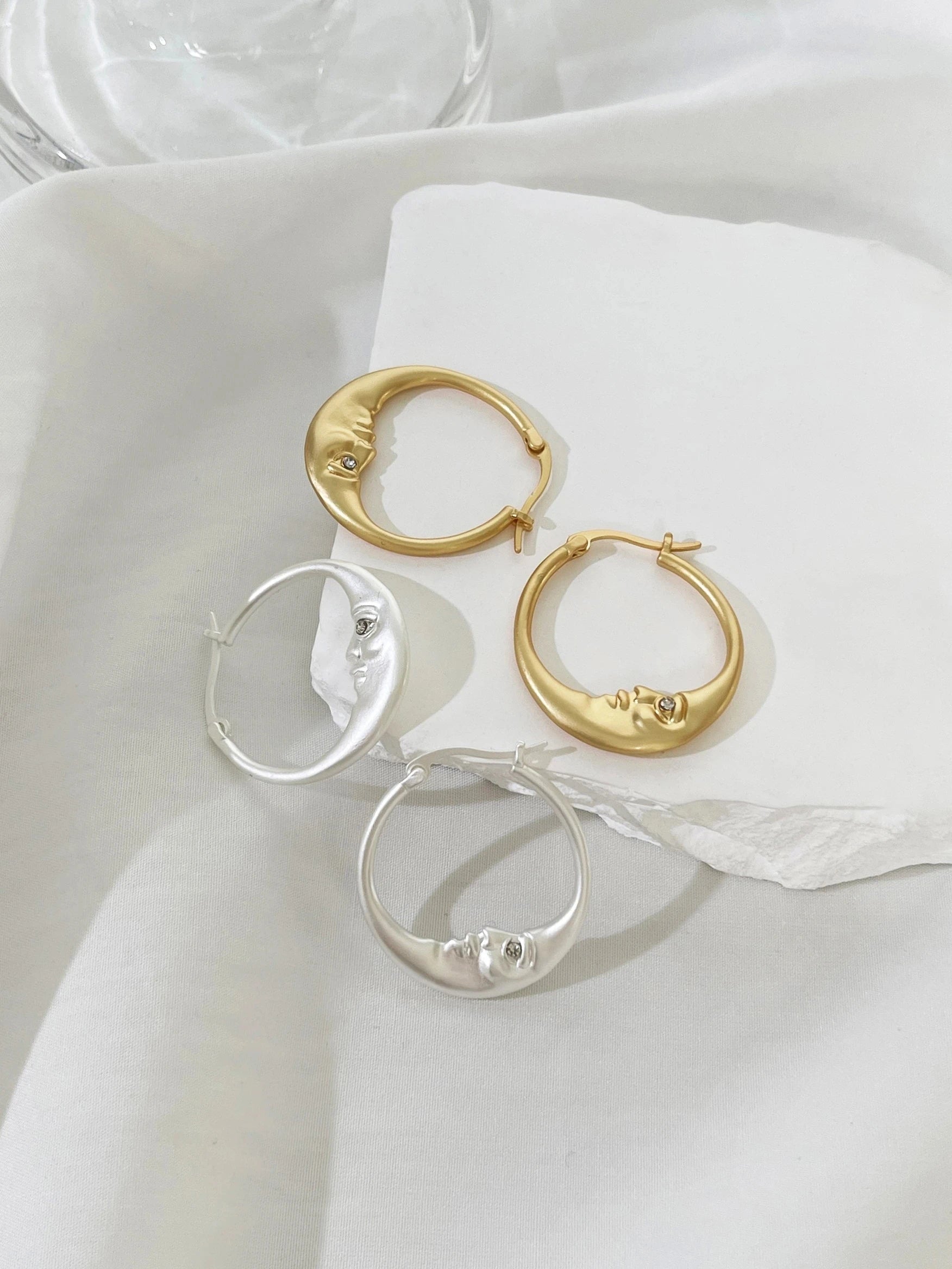 Gold and silver hoop earrings on a white fabric background