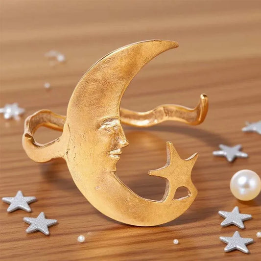Gold moon and star brooch on a wooden surface with decorative stars and pearls.