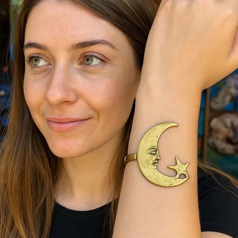 Woman wearing a gold crescent moon and star bracelet, smiling outdoors.