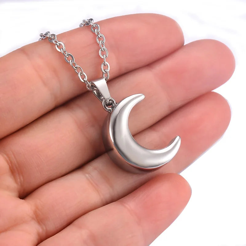 Silver crescent moon necklace held in a hand against a white background
