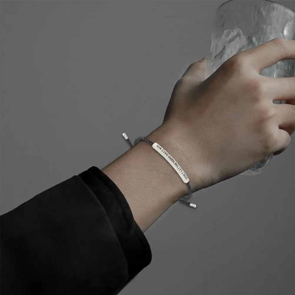 Hand wearing a silver bracelet with engraved text on a dark background