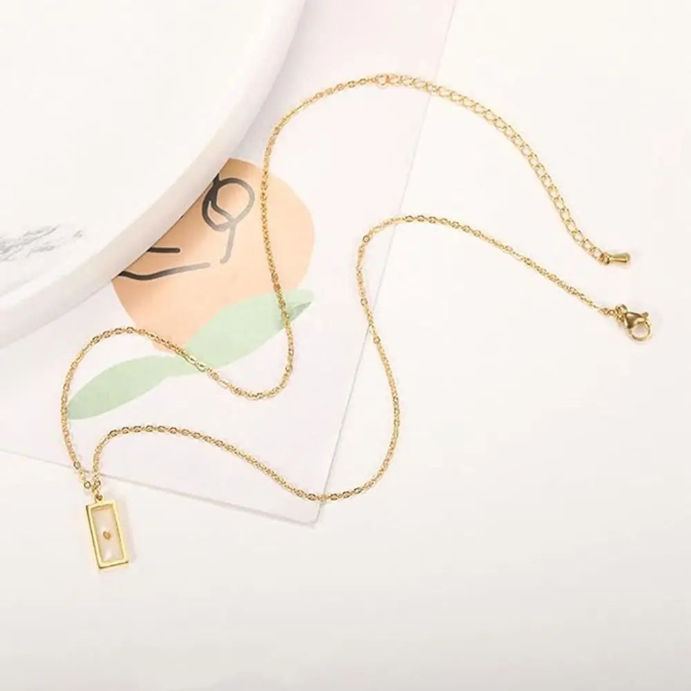 Gold necklace with a rectangular pendant on a white surface