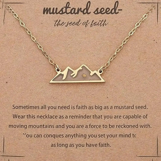 Gold necklace with a mountain silhouette pendant on a brown kraft card that reads 'mustard seed- the seed of faith' with inspirational text below.
