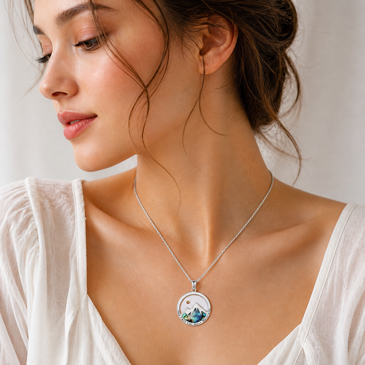 Woman wearing a necklace with a scenic pendant against a light background