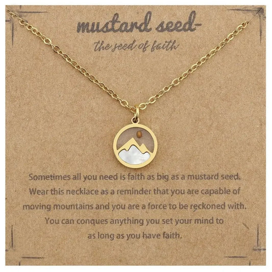 A gold-tone necklace with a circular pendant displayed on a brown kraft card. The pendant features a white inlay shaped like a mustard seed and small mountain-like shapes.