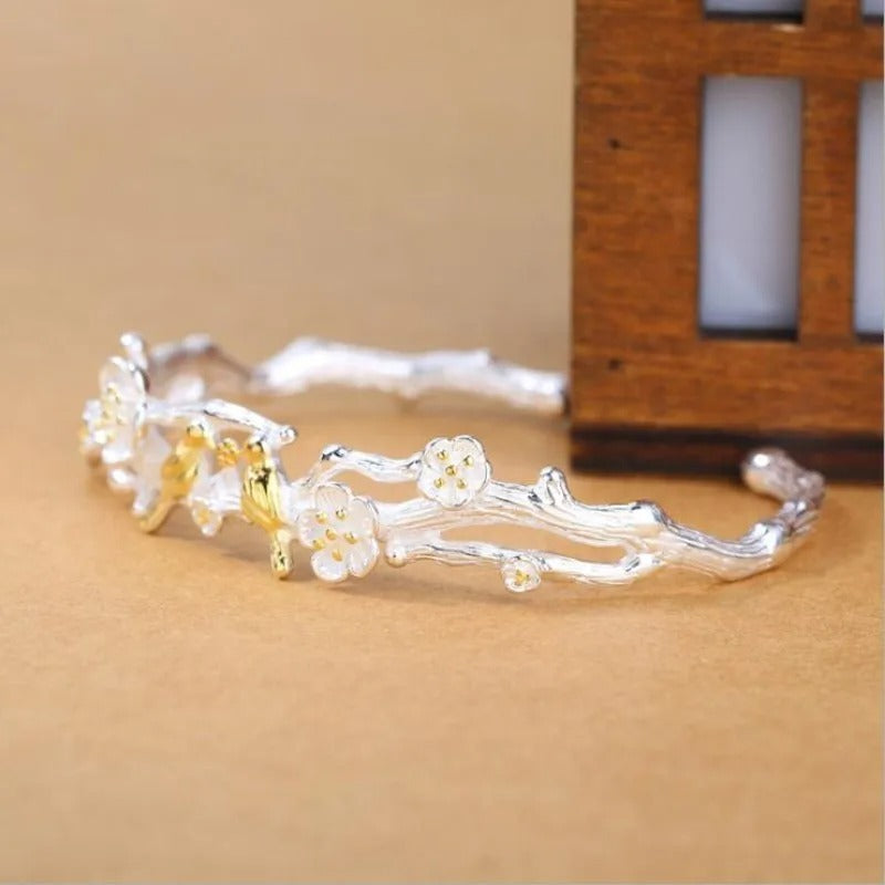 Silver and gold bracelet with floral designs on a beige background