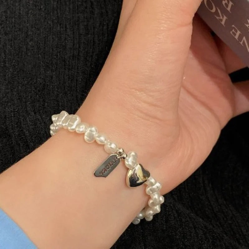 Pearl bracelet with a heart-shaped tag on a wrist against a dark background