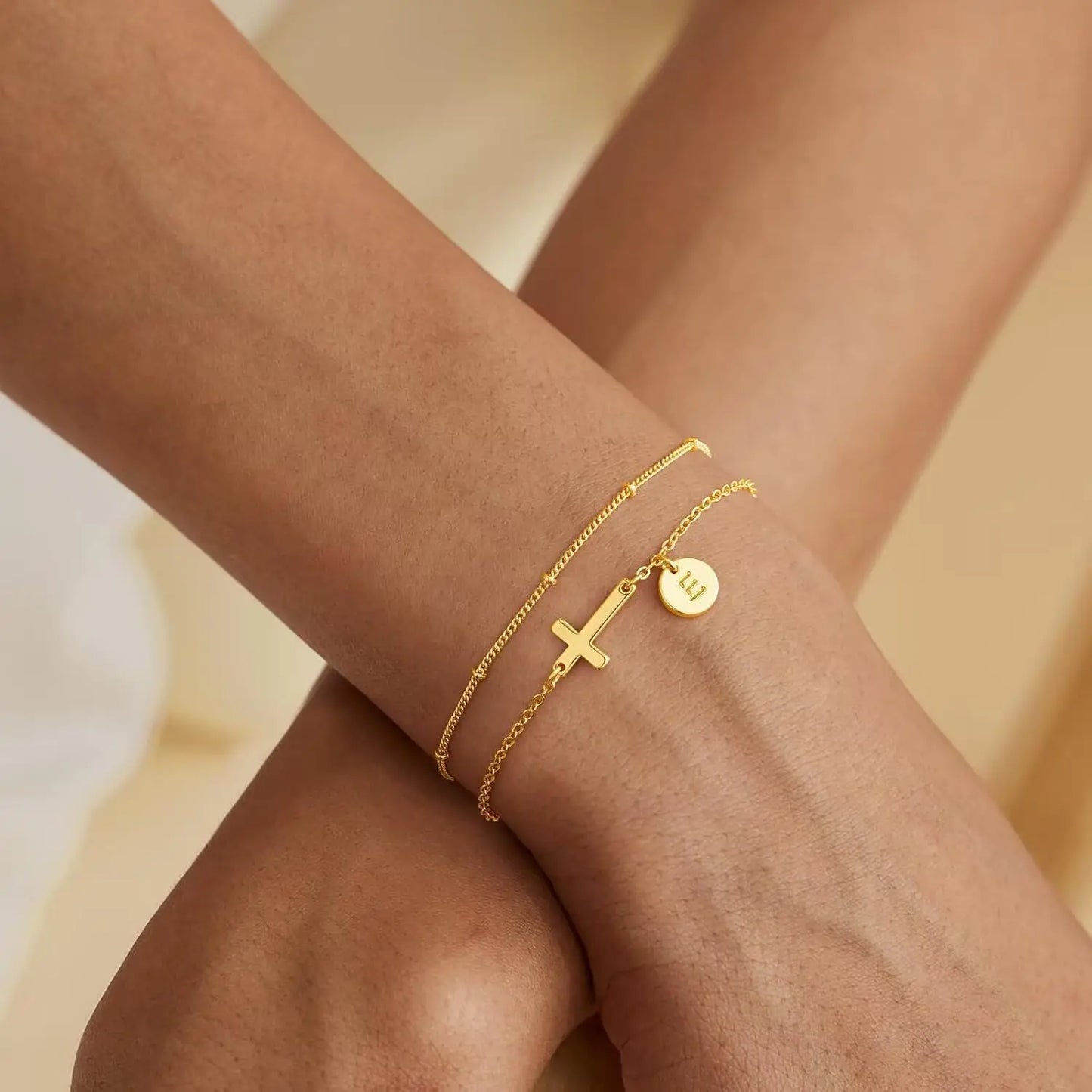 Gold bracelets on a person's wrist against a beige background