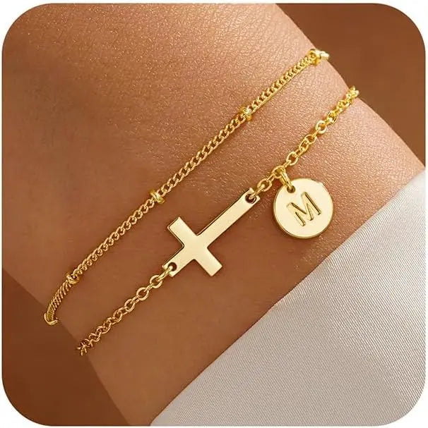 Gold bracelet with cross and circular charm on a skin-toned surface