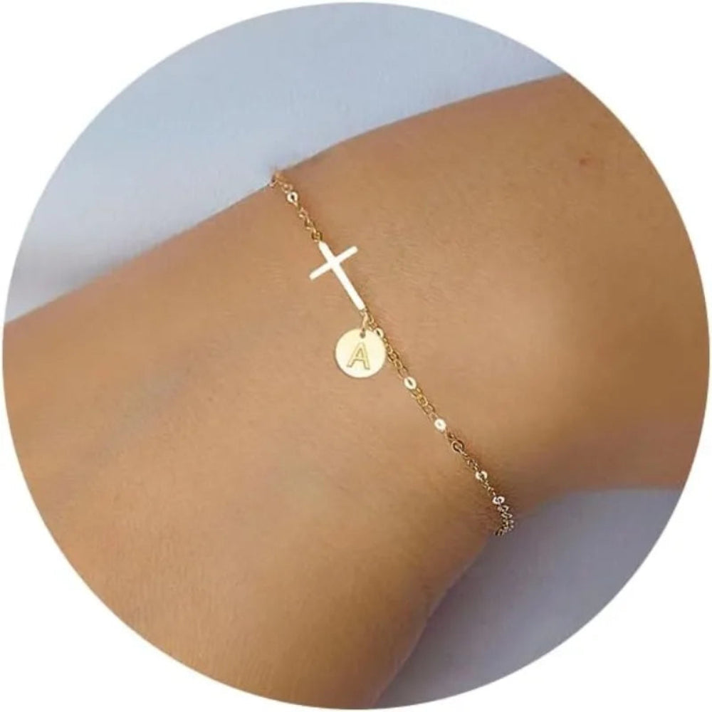 Gold bracelet with a cross and letter 'A' charm on a person's ankle.