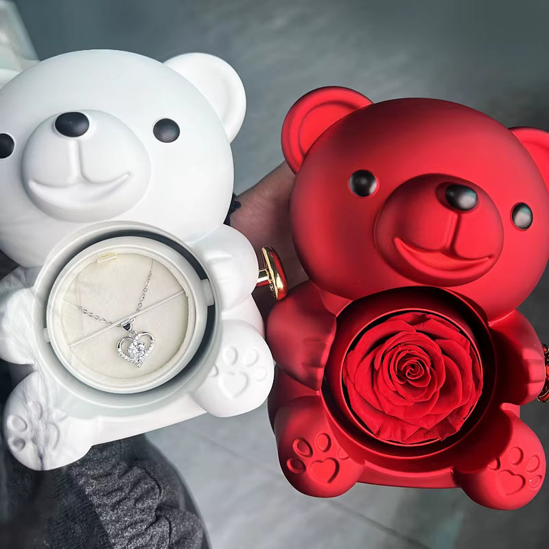 White teddy bear with a necklace and red teddy bear with a rose inside, held by a hand.